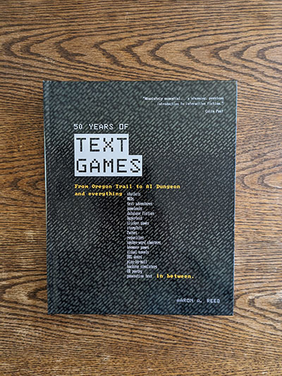The hardcover edition of 50 Years of Text Games standing upright against a neutral background. It features a black faux-leather cover, with the title overlaid in silver foil and the debossed years 1971 and 2020.